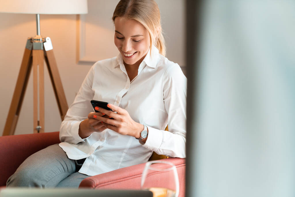Jolie femme d'affaires blonde joyeuse s'asseoir à l'intérieur dans un café en utilisant un téléphone mobile
. - Photo, image