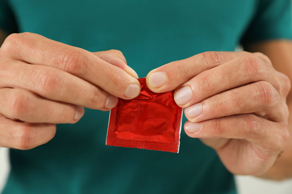 Młody człowiek otwiera prezerwatywę, zbliżenie. Koncepcja bezpiecznego seksu - Zdjęcie, obraz