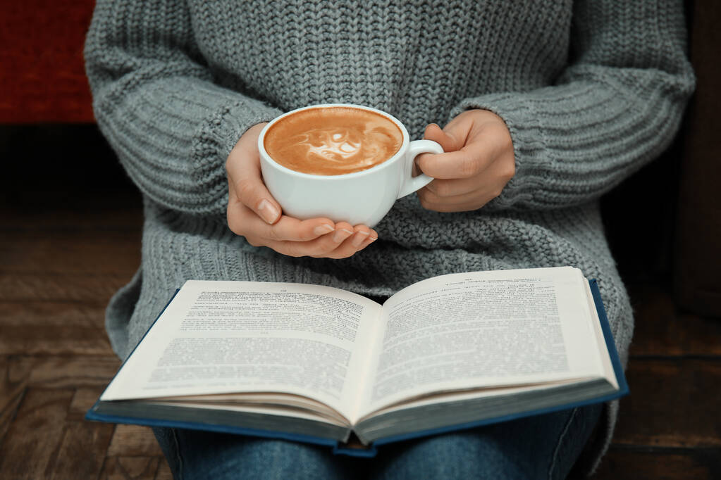 Vrouw met kopje koffie lezen boek thuis, close-up - Foto, afbeelding