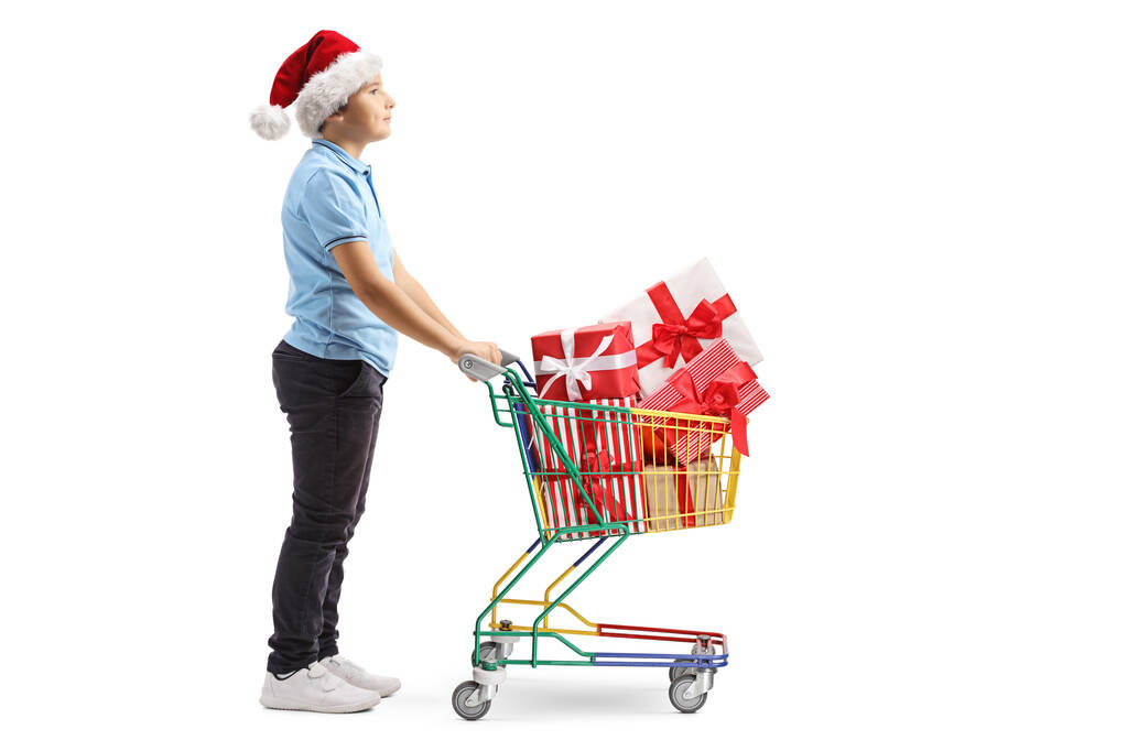 Ragazzo con un cappello di Babbo Natale spingendo un mini carrello della spesa con pre
 - Foto, immagini