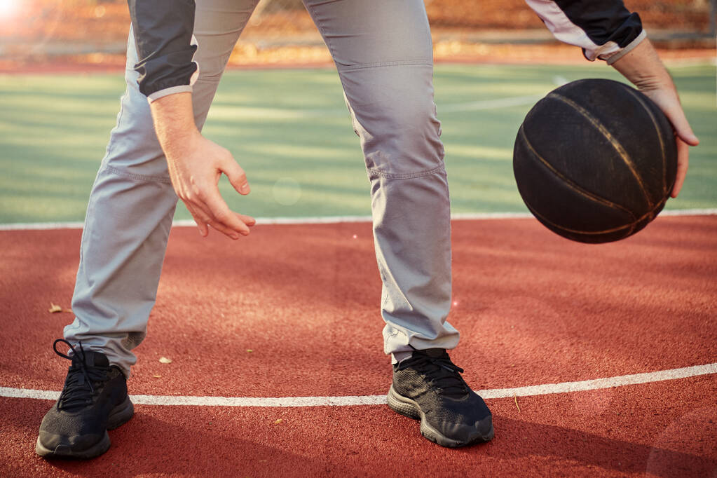 Молодой человек на баскетбольной площадке капает мячом. Стритбол, тренировки, активность. Настоящее и подлинное, винтажное настроение
. - Фото, изображение