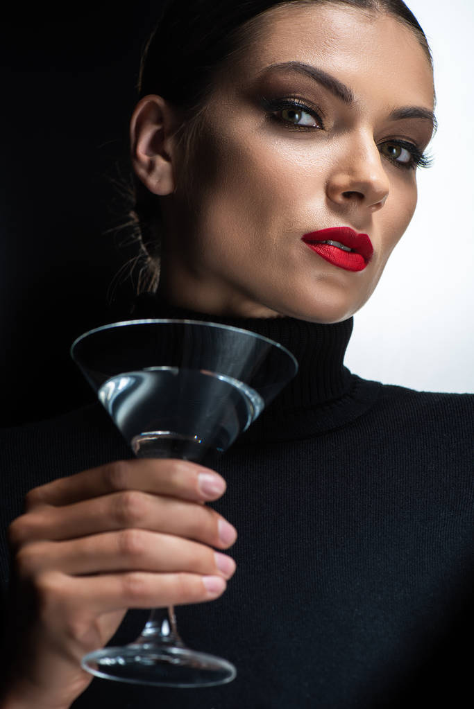 mooie elegante vrouw met rode lippen houden martini en kijken naar camera geïsoleerd op wit en zwart - Foto, afbeelding