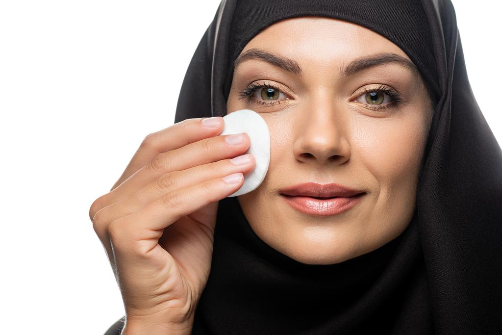 mosolygós fiatal muszlim nő hidzsáb törölgetés arc pamut pad elszigetelt fehér - Fotó, kép