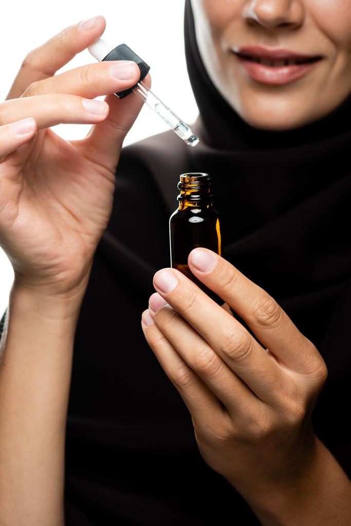 vista parziale di giovane donna musulmana in hijab tenendo contagocce una bottiglia con siero isolato su bianco
 - Foto, immagini