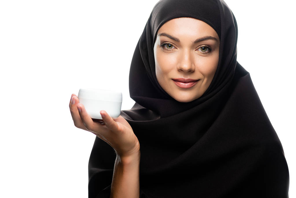 Улыбающаяся мусульманка в хиджабе держит контейнер с косметическим кремом, изолированным на белом
 - Фото, изображение