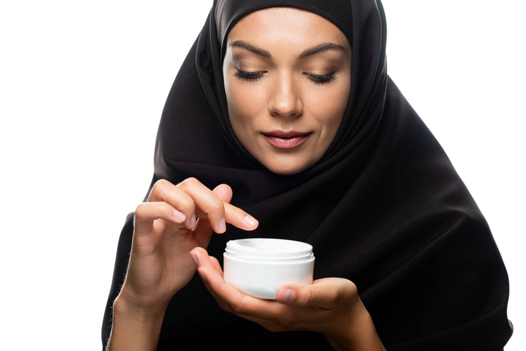 Молода мусульманка в Хіджабі, яка тримає контейнер з косметичним кремом ізольованим на білому. - Фото, зображення