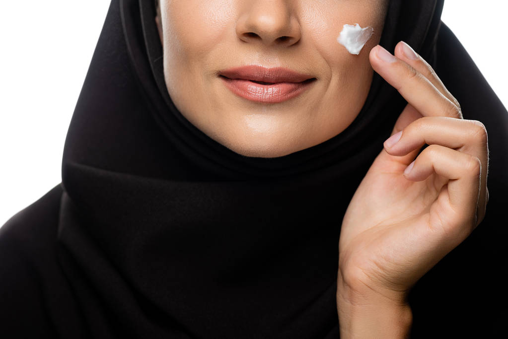 обрезанный вид молодой мусульманки в хиджабе с нанесением косметического крема на цыпленка, изолированного на белом
 - Фото, изображение