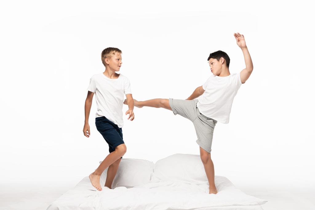 хлопчик жартома штовхає брата з ногою, розважаючись на ліжку ізольовано на білому
 - Фото, зображення
