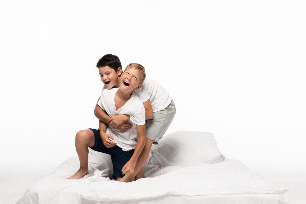cheerful boys imitating fighting while having fun on bed isolated on white - Photo, Image