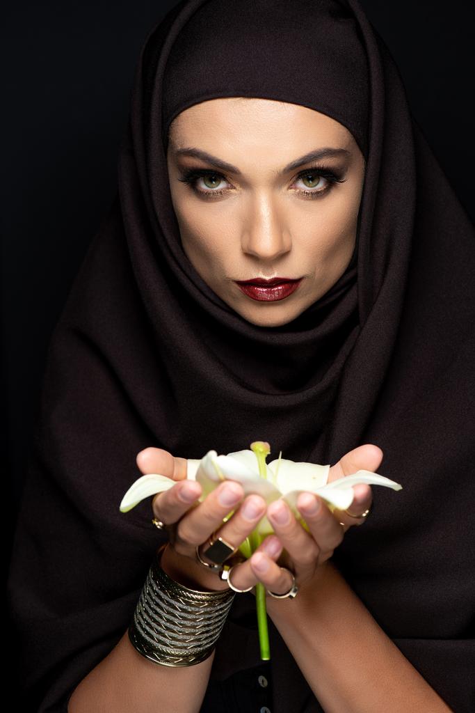 gyönyörű muszlim nő hidzsáb arany gyűrűk és karkötő gazdaság liliom elszigetelt fekete - Fotó, kép