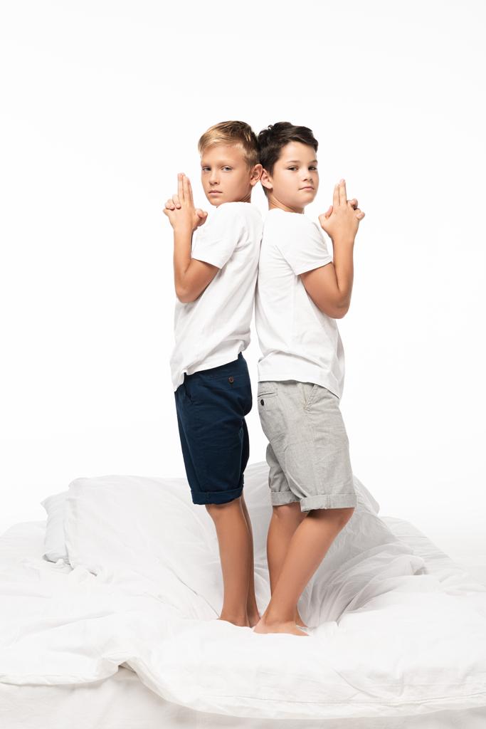 due ragazzi in piedi schiena contro schiena sul letto e mostrando gesti di pistola isolati su bianco
 - Foto, immagini