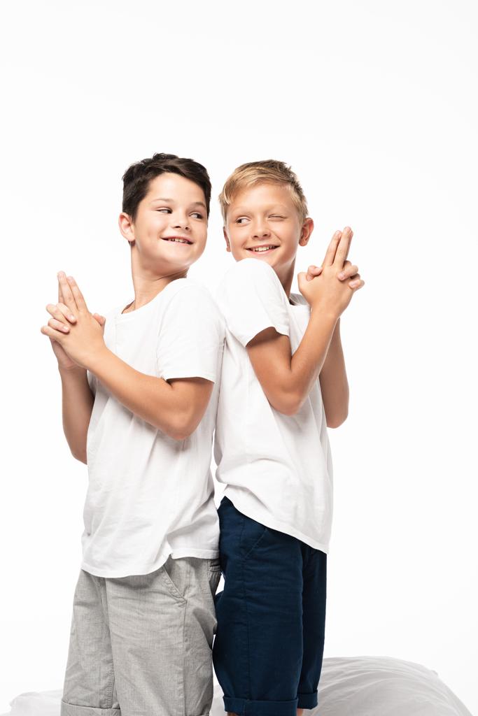 dos hermanos alegres de pie espalda con espalda y mostrando gestos de armas aislados en blanco
 - Foto, Imagen