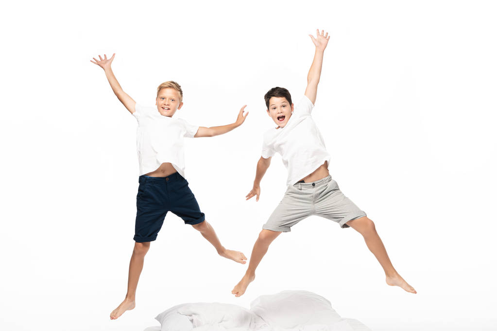 dva nadšení bratři vznášející se nad postelí a dívající se na kameru izolovanou na bílém - Fotografie, Obrázek