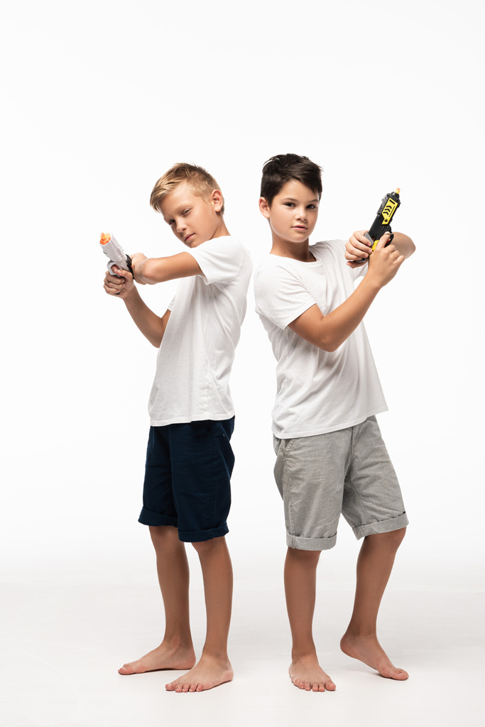 dwóch braci stojących plecami do siebie, trzymających zabawki i patrzących w obiektyw na białym tle - Zdjęcie, obraz