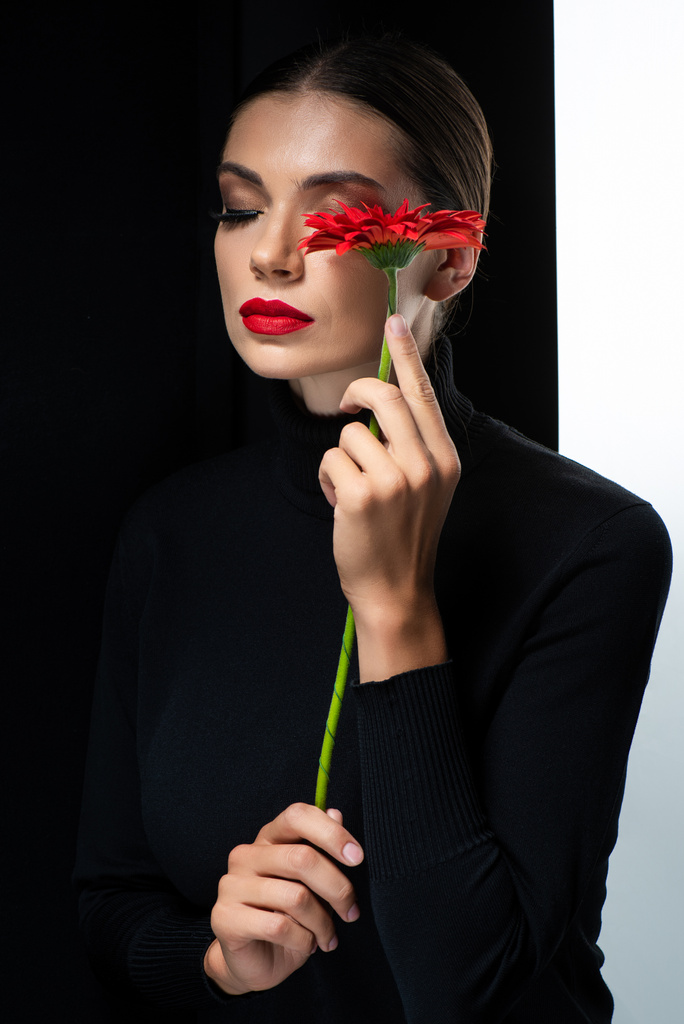 hermosa mujer con labios rojos y ojos cerrados sosteniendo gerberas rojas aisladas en blanco y negro
 - Foto, imagen