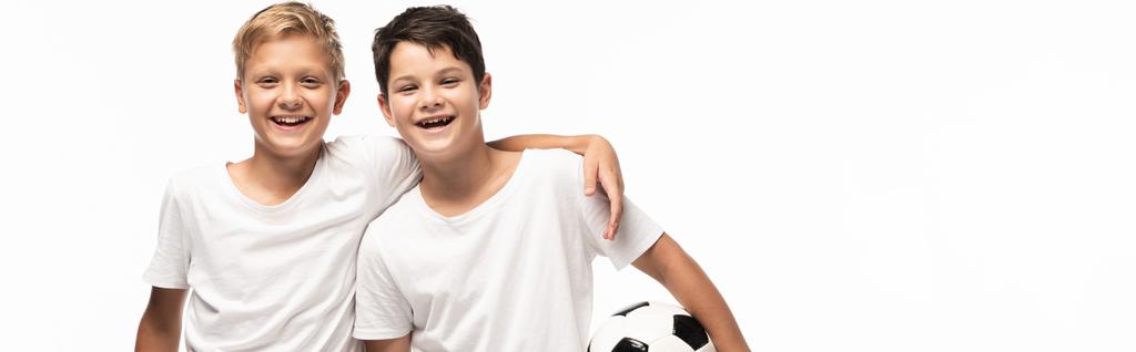 panoramiczny strzał szczęśliwy chłopiec przytulanie brat trzyma piłkę nożną odizolowany na biały - Zdjęcie, obraz