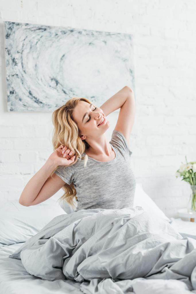 fröhliche Frau lächelt beim Aufwachen im Schlafzimmer  - Foto, Bild