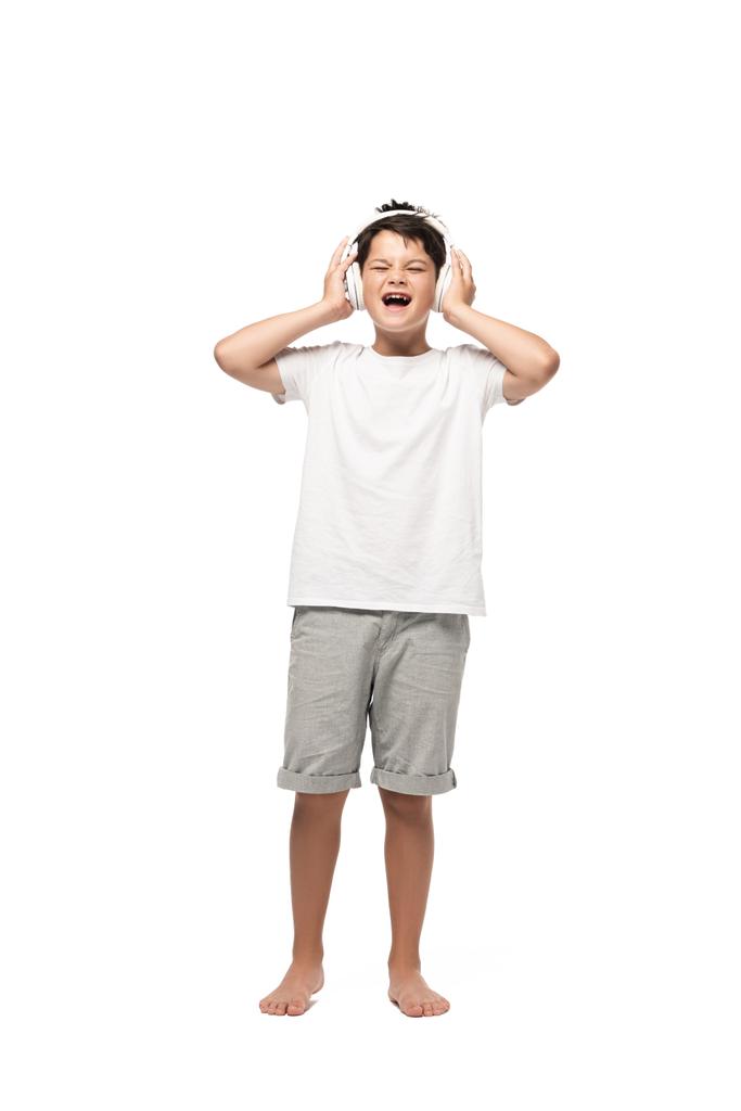 excited boy holding hands on headphones and singing while listening music on white background - Photo, Image