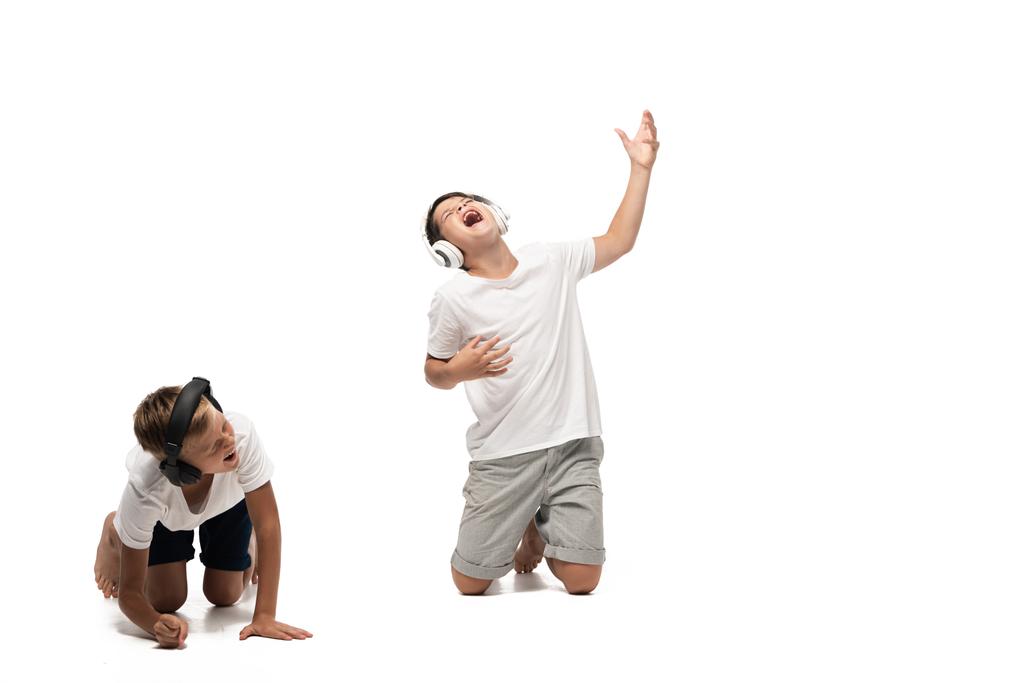 niño emocionado escuchando música en los auriculares y cantando cerca hermano riendo sobre fondo blanco
 - Foto, imagen