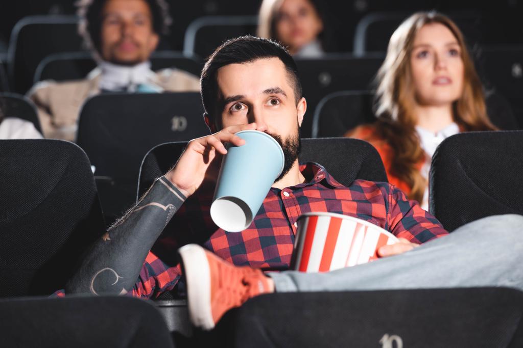 szelektív fókusz jóképű férfi ivás szóda és filmet nézni a moziban  - Fotó, kép