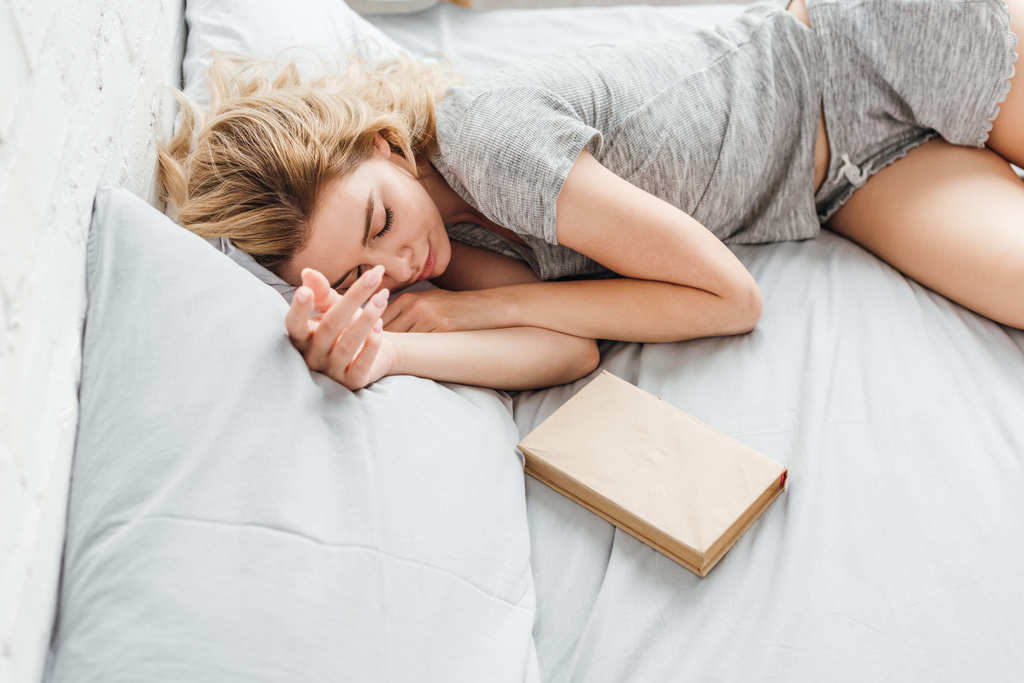 Вид на девочку, спящую возле книги на кровати
  - Фото, изображение