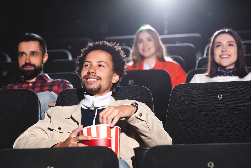 foyer sélectif de sourire homme afro-américain tenant du pop-corn et regarder des films au cinéma
  - Photo, image