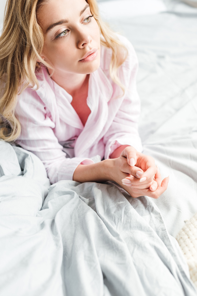 ελκυστική κοπέλα ξαπλωμένη με σφιγμένα χέρια στο κρεβάτι  - Φωτογραφία, εικόνα