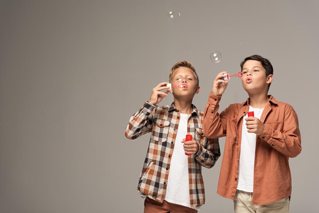 dwa słodkie chłopcy dmuchanie bańki mydlane izolowane na szary - Zdjęcie, obraz