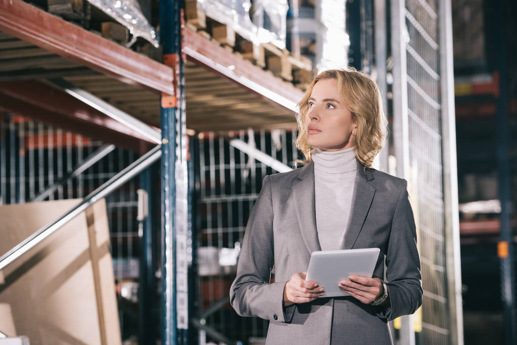 confident businesswoman holding digital tablet while looking away in warehouse - 写真・画像