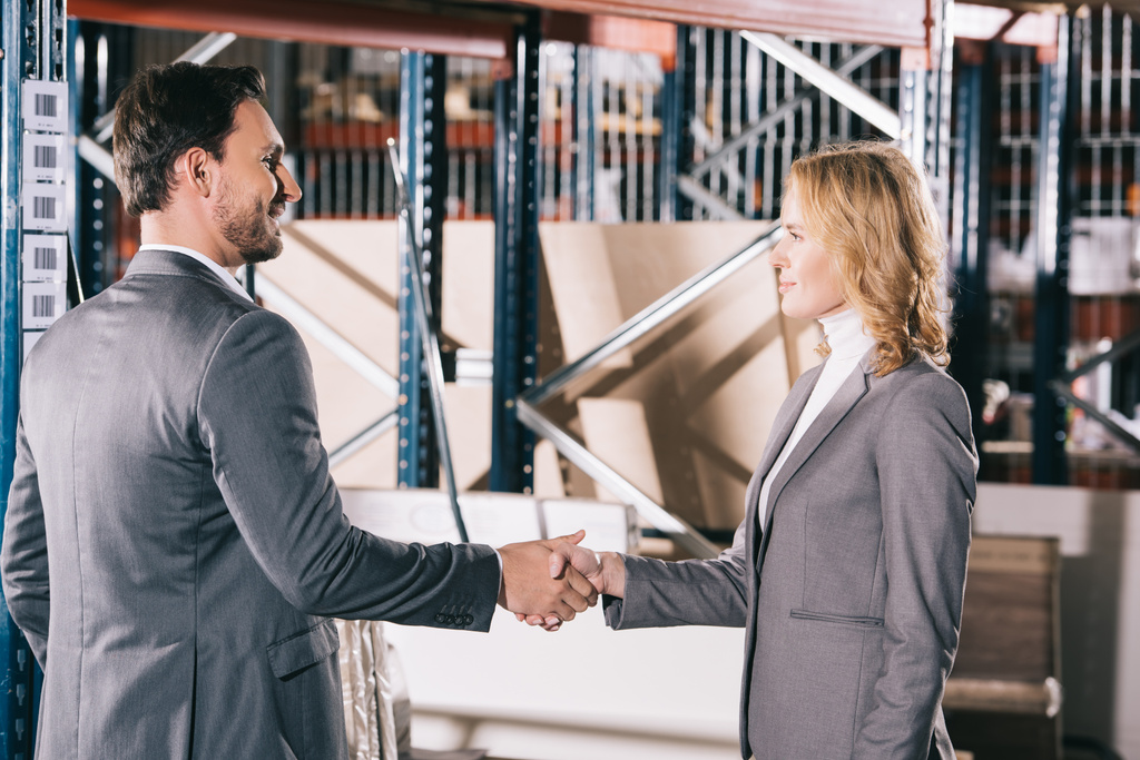 smiling businessman and businesswoman shaking hands in warehouse - Photo, Image