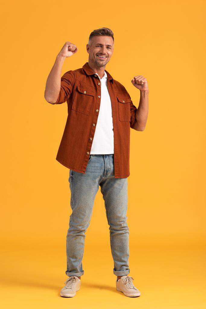 fröhlicher Mann mit geballten Fäusten auf orangefarbenem Hintergrund  - Foto, Bild