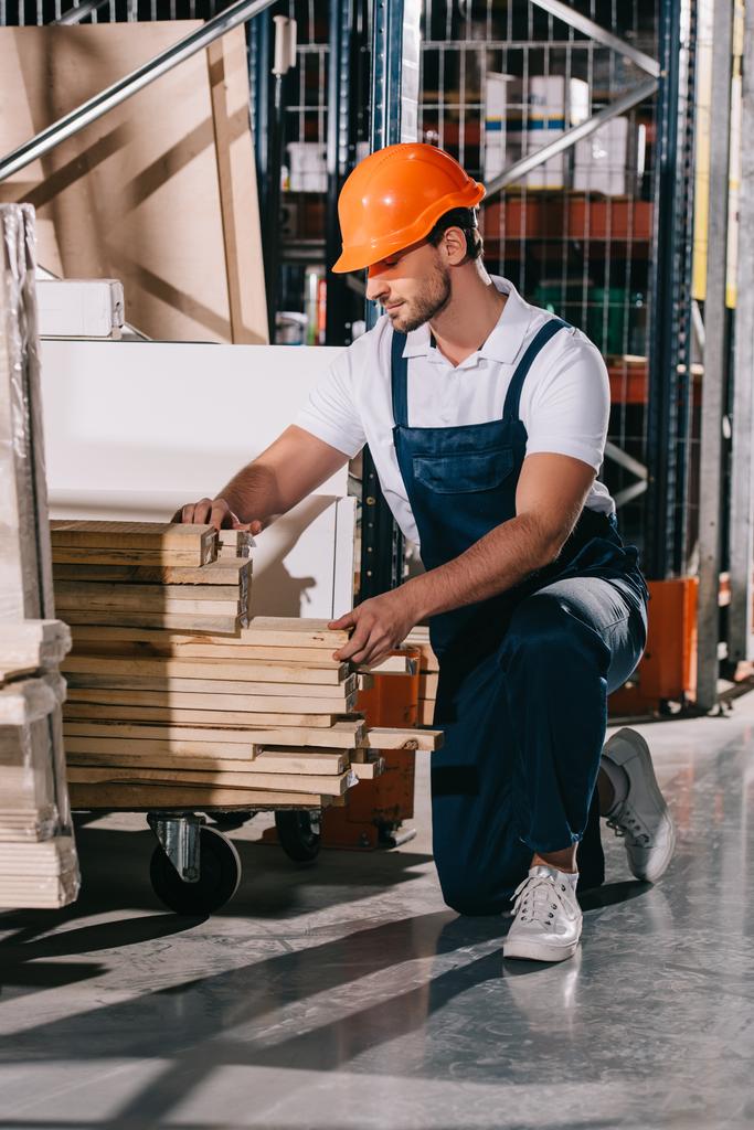 ouvrier d'entrepôt debout sur le genou près du rack avec des planches en bois
 - Photo, image