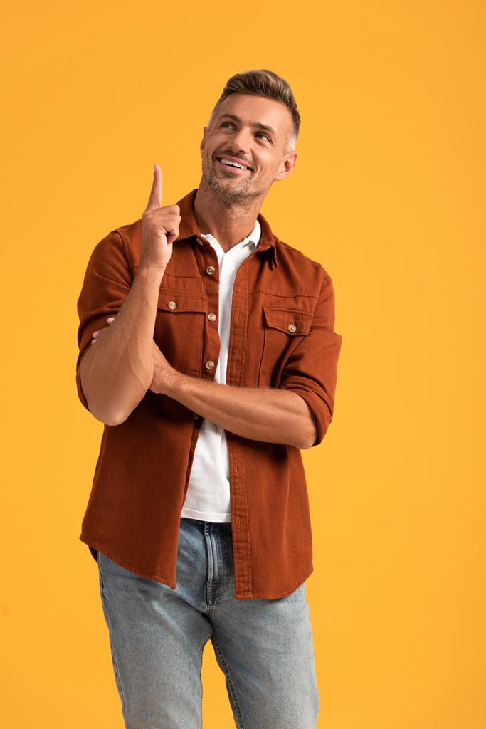 homem alegre apontando com o dedo e olhando para cima isolado em laranja
  - Foto, Imagem