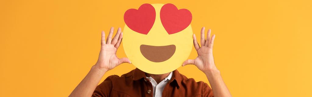 KYIV, UCRANIA - 24 DE SEPTIEMBRE DE 2019: plano panorámico del hombre cubriendo la cara con ojos de corazón emoticono de dibujos animados aislados en naranja
  - Foto, imagen