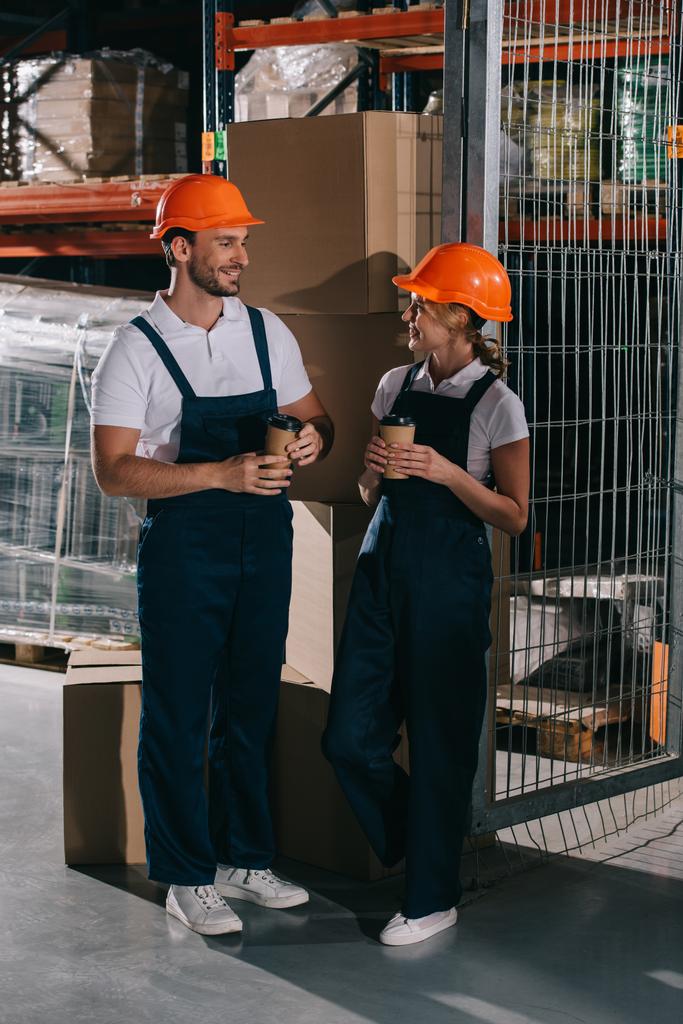 smiling warehouse workers looking at each other while holding coffee to go - Photo, Image