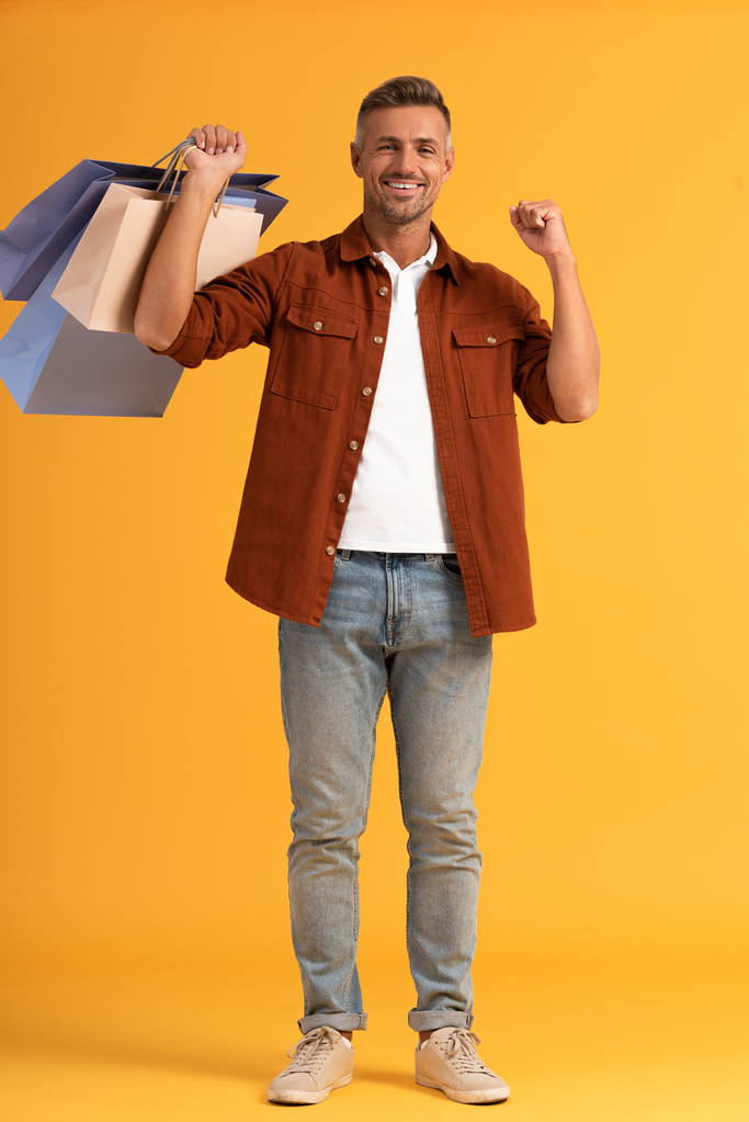 χαρούμενος άνθρωπος κρατώντας πολύχρωμες τσάντες ψώνια σε πορτοκαλί  - Φωτογραφία, εικόνα