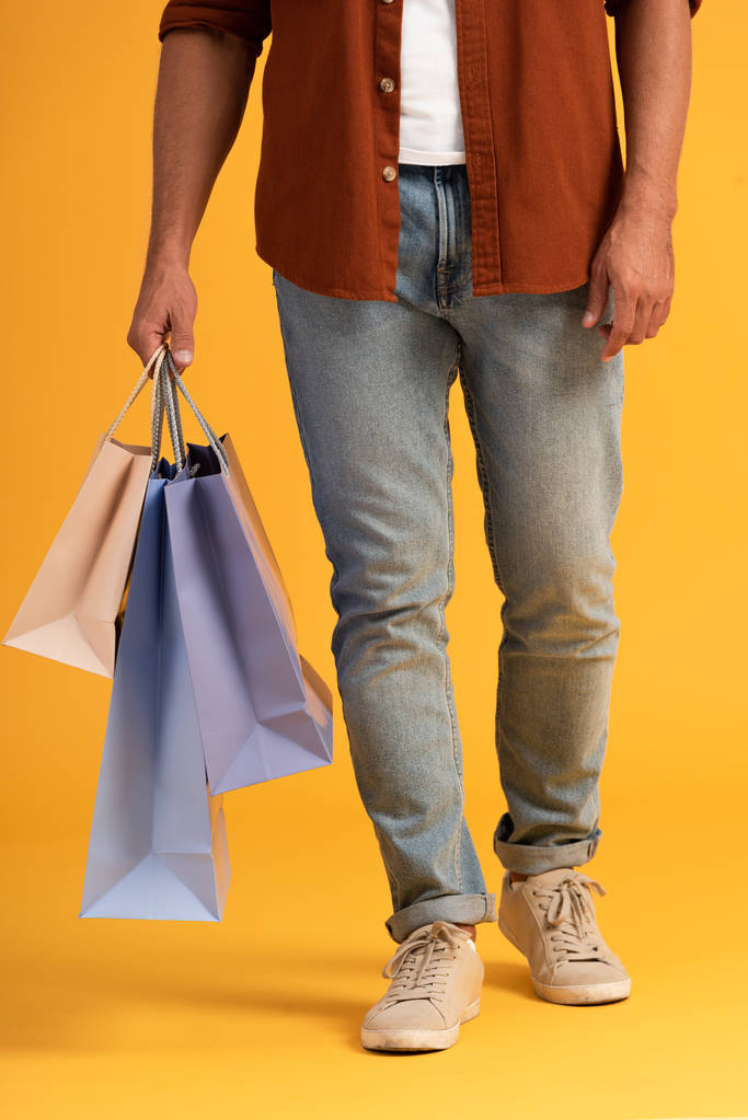 vista recortada del hombre de pie con bolsas de compras en naranja
  - Foto, imagen