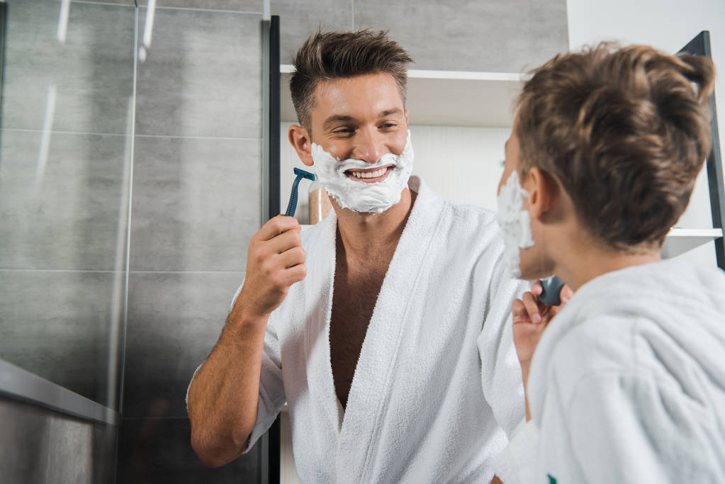 избирательный фокус счастливого отца с пеной для бритья на лице глядя на сына в ванной комнате
  - Фото, изображение