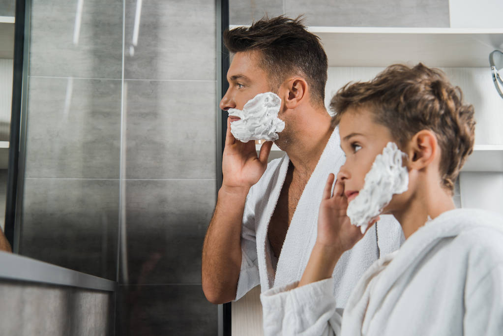 selektivní zaměření otce nanášení pěny na holení na obličej blízko syna v koupelně  - Fotografie, Obrázek