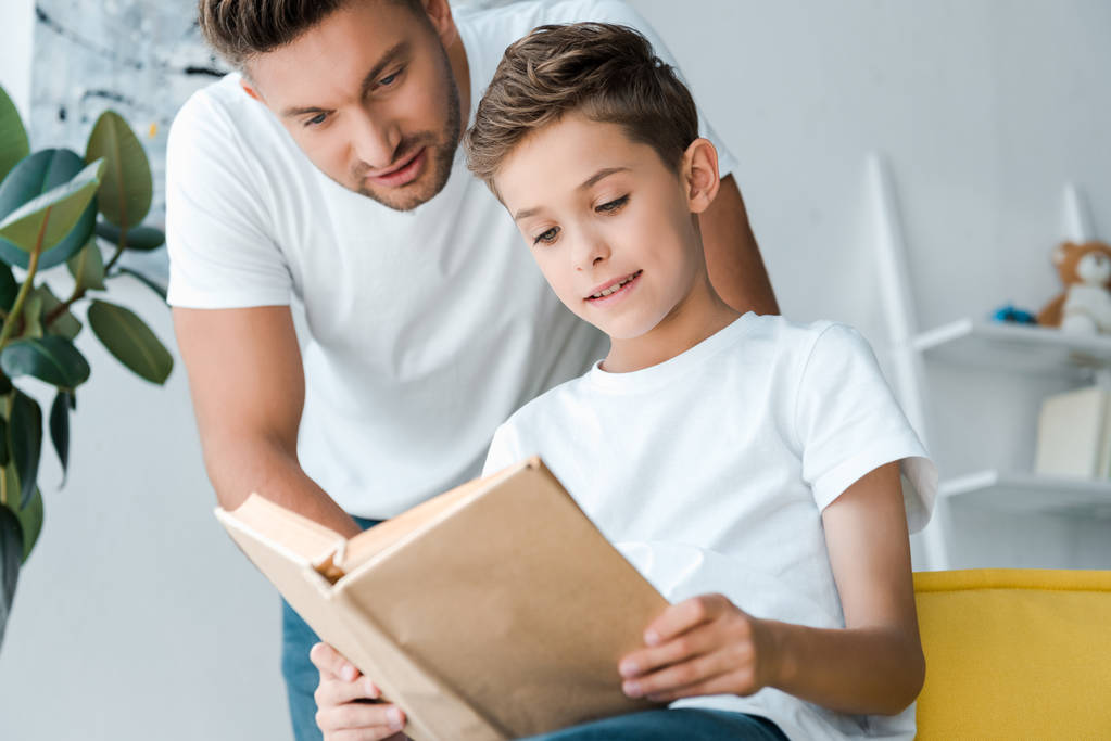 selective focus of father standing near cute son holding book - Photo, Image