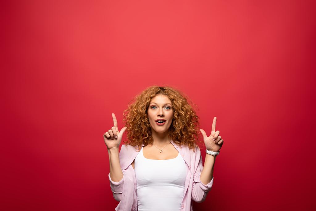 beautiful excited redhead woman pointing up, isolated on red - Photo, Image