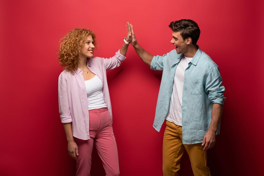 mooi gelukkig paar in casual kleding geven high five, geïsoleerd op rood - Foto, afbeelding