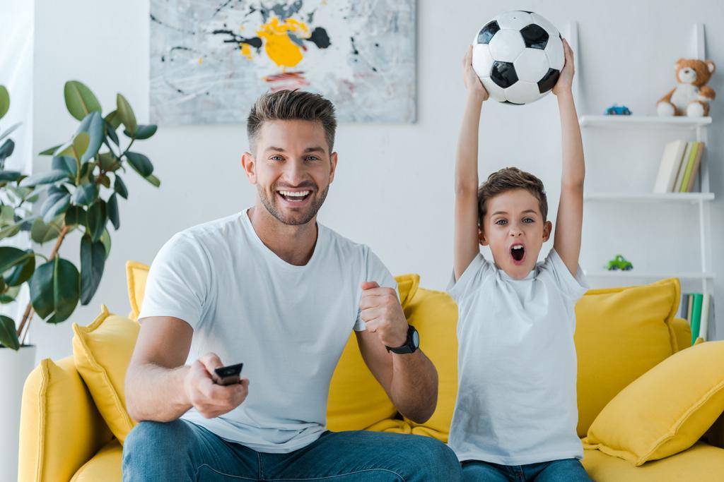 joyeux père tenant télécommande près du fils avec football au-dessus de la tête
  - Photo, image