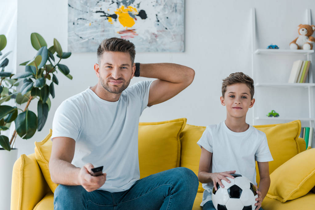 knappe vader houden afstandsbediening in de buurt van zoon met voetbal  - Foto, afbeelding