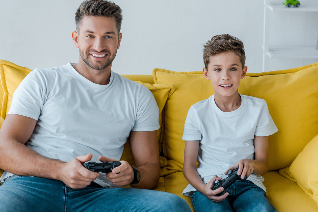 Kyiv,ウクライナ- 2019年10月2日:幸せな父親と息子が自宅でビデオゲームをプレイ  - 写真・画像