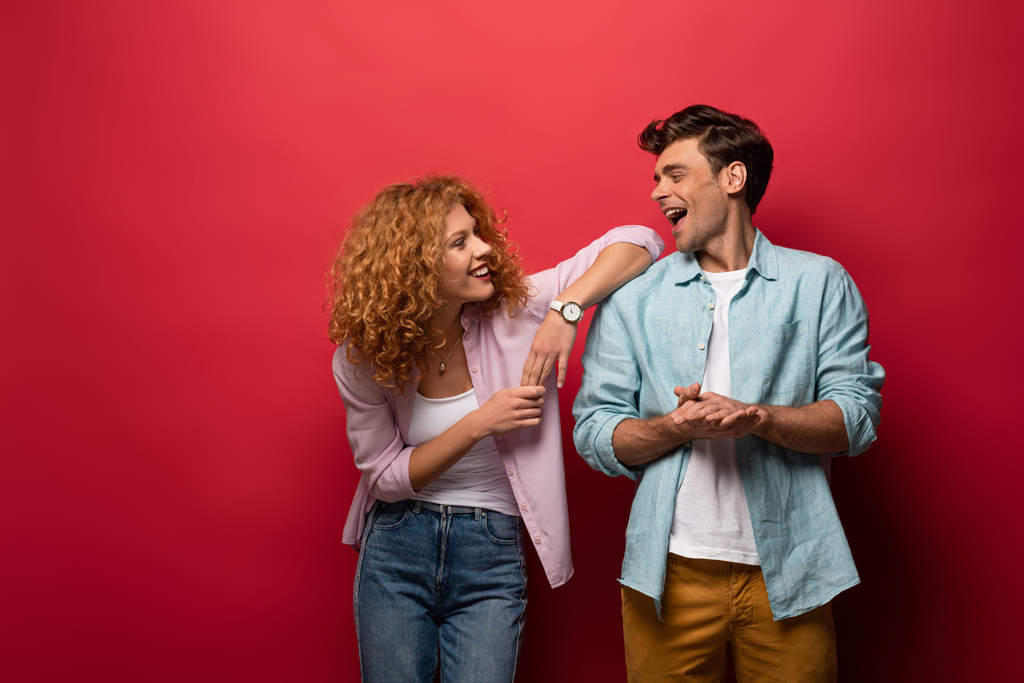 happy couple laughing in casual clothes isolated on red - Photo, Image