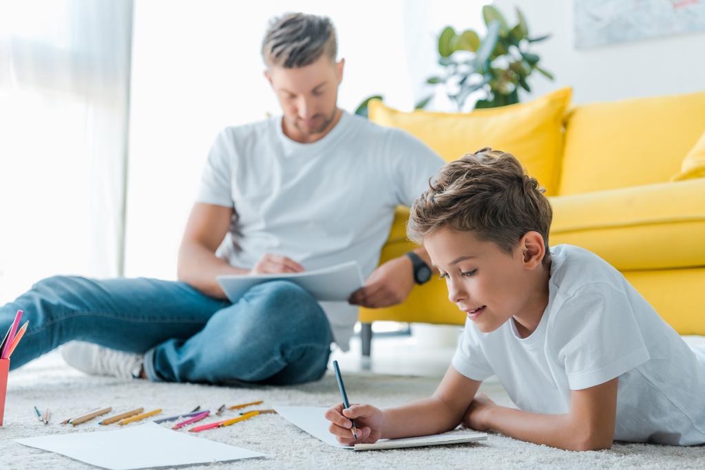 вибірковий фокус щасливої дитини, що малює біля красивого батька вдома
  - Фото, зображення