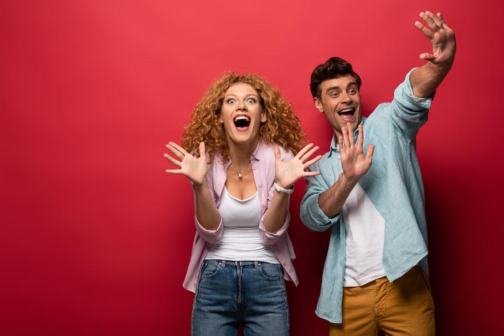 beautiful excited couple gesturing in casual clothes isolated on red - Photo, Image