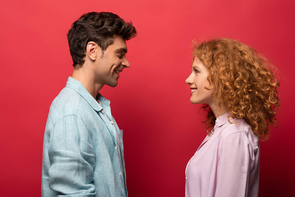 beautiful happy couple in casual clothes looking at each other isolated on red - Photo, Image