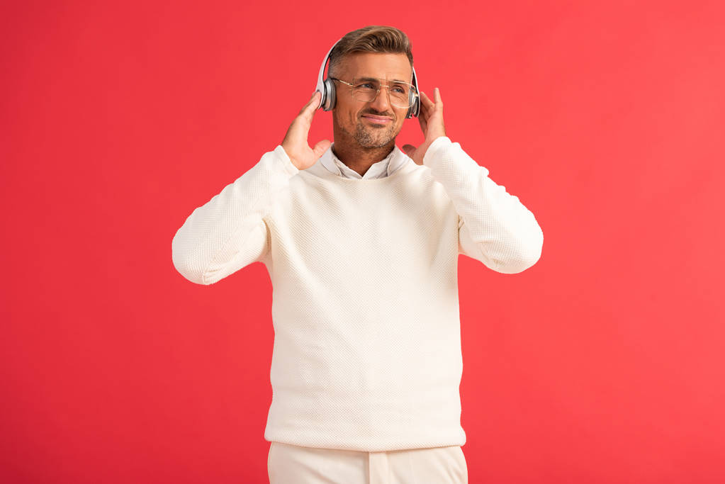 niezadowolony człowiek słuchanie muzyki w słuchawkach bezprzewodowych izolowanych na czerwono  - Zdjęcie, obraz